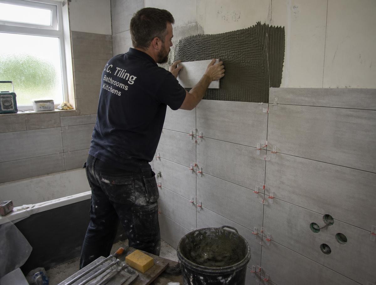 Bathroom fitter tiling a wall during a UK bathroom renovation