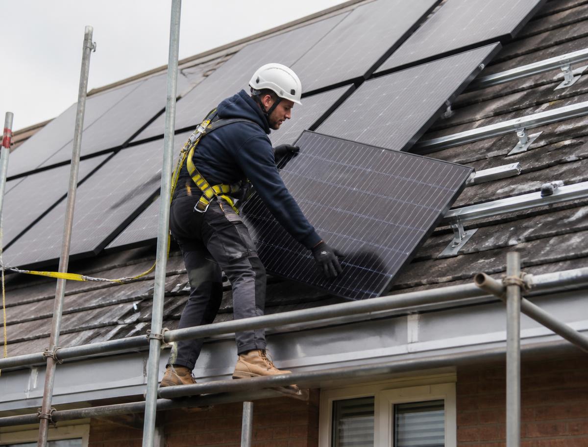 Installer fitting solar panels on a UK roof from scaffolding